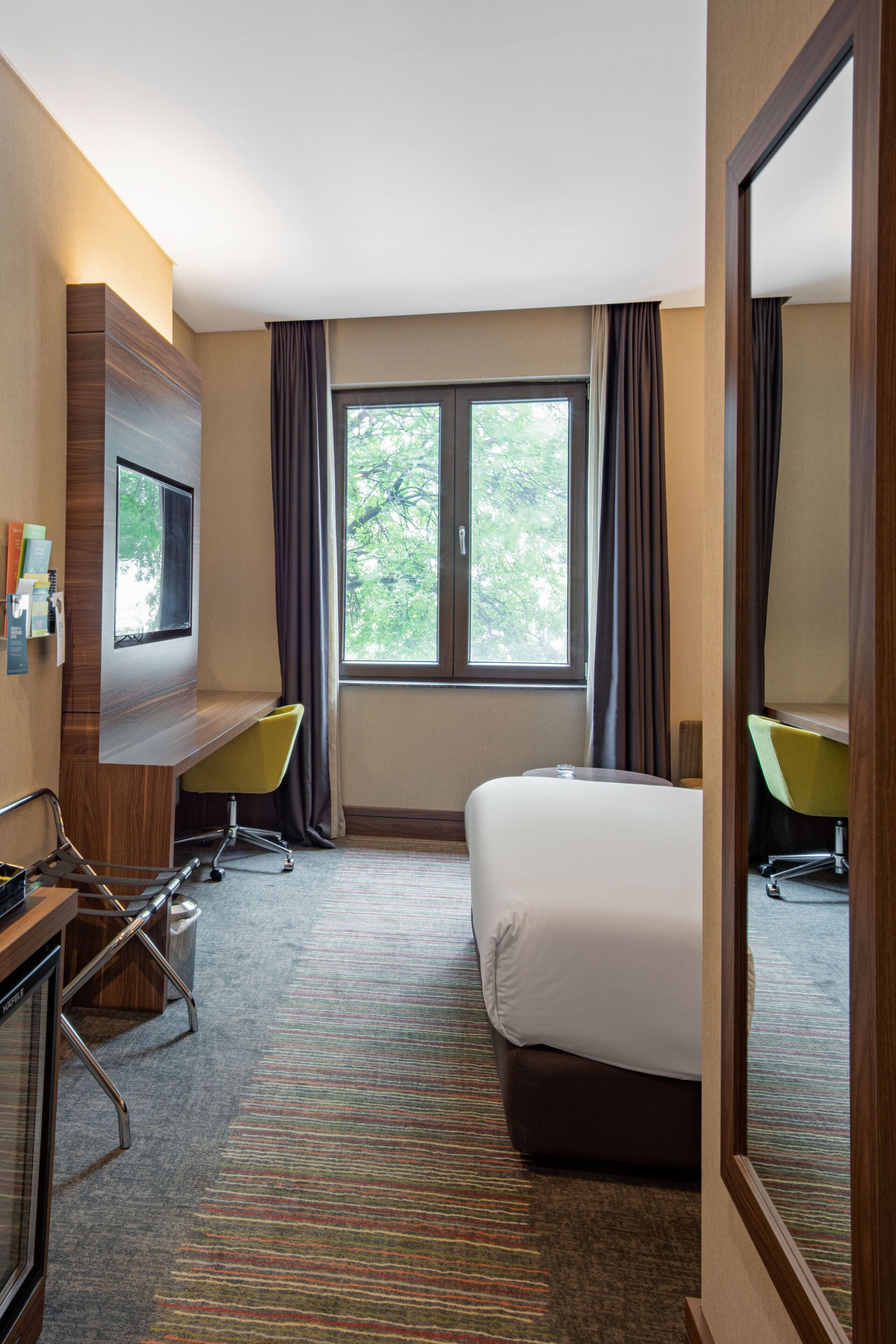 A hotel room with a bed, a desk, a chair, a TV, and a window with curtains.