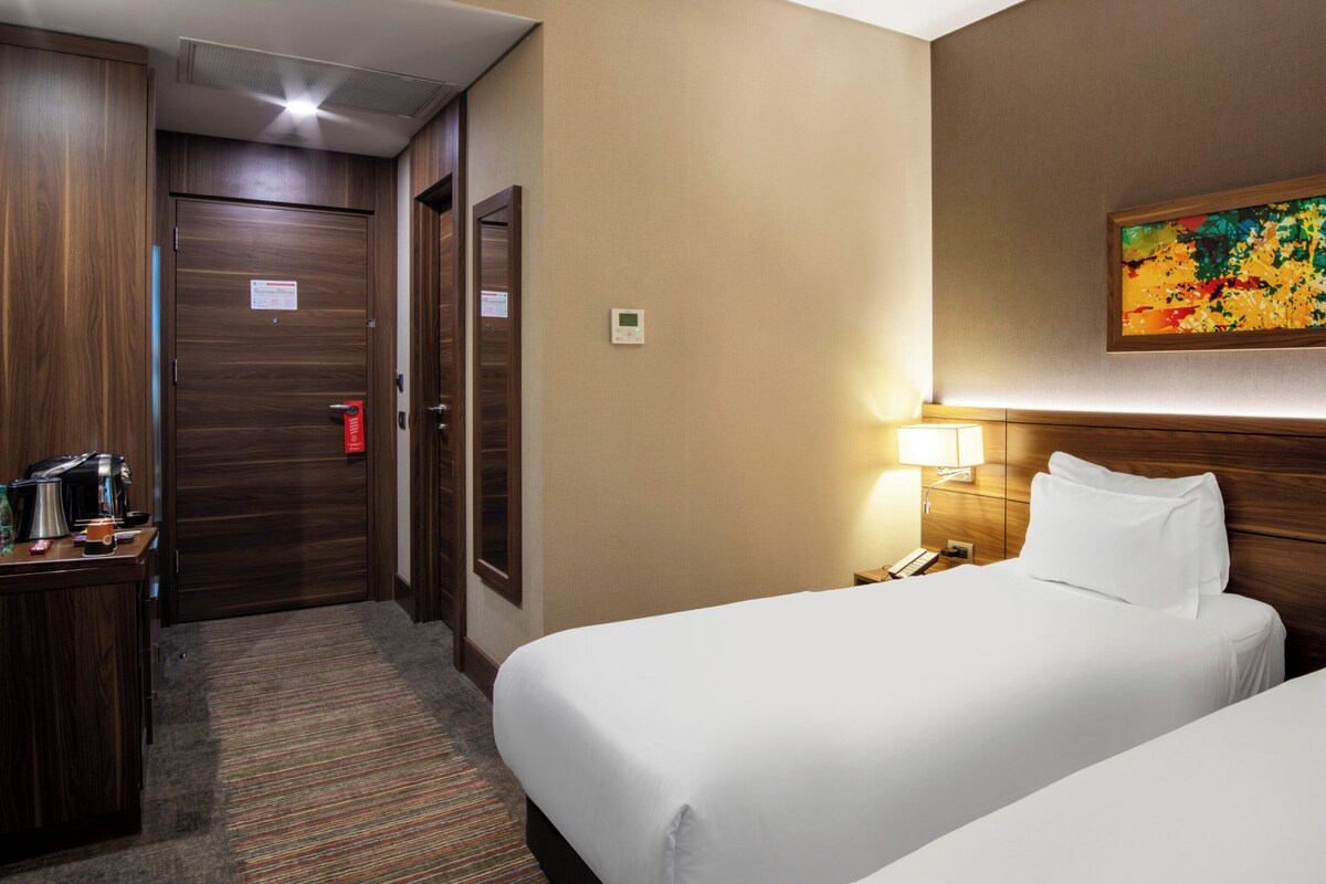 Een hotelkamer met twee bedden, een bureau met koffiezetapparaat, een telefoon en een schilderij aan de muur.