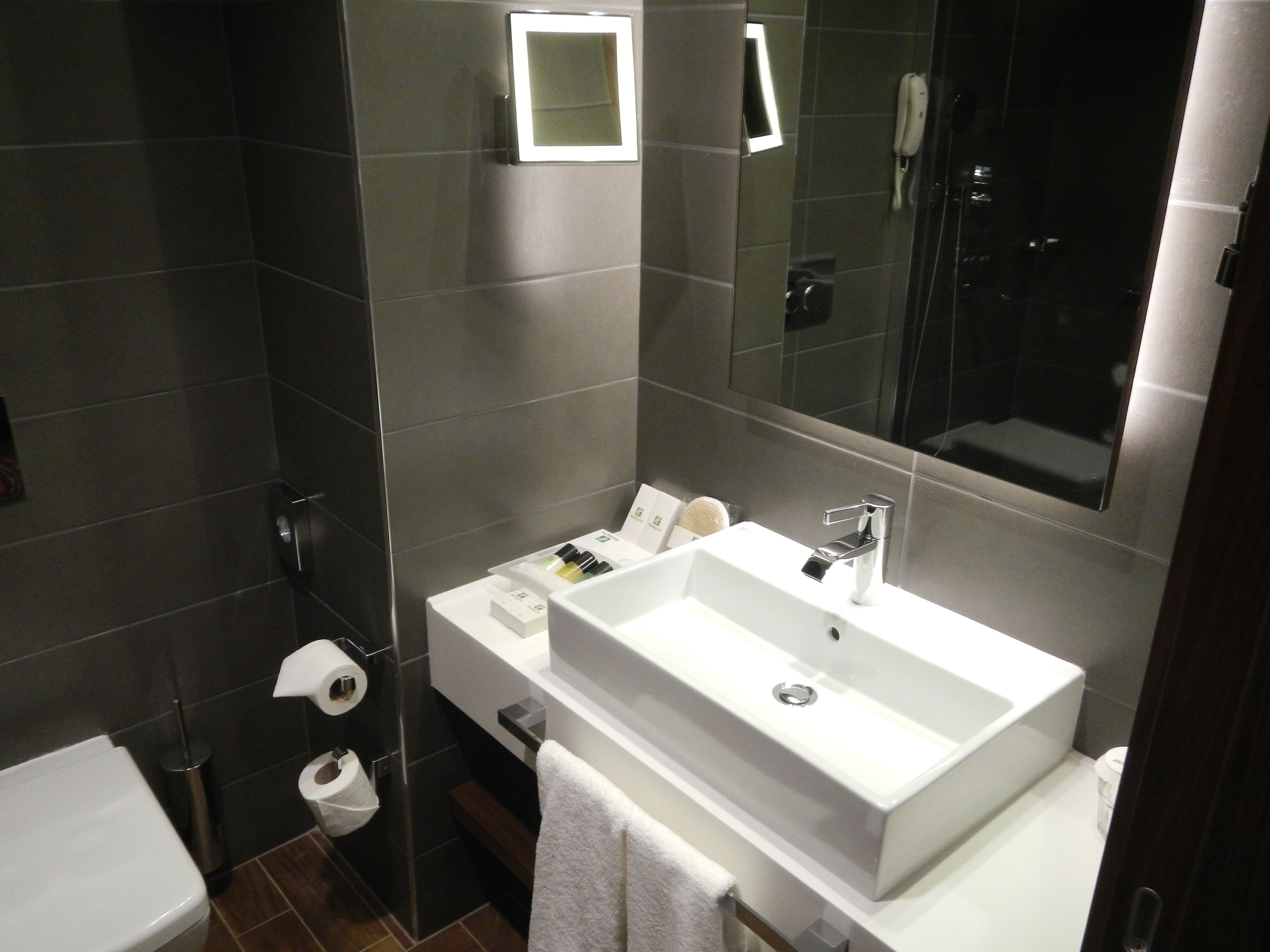 A modern bathroom with a large sink, mirror, and a shower area.