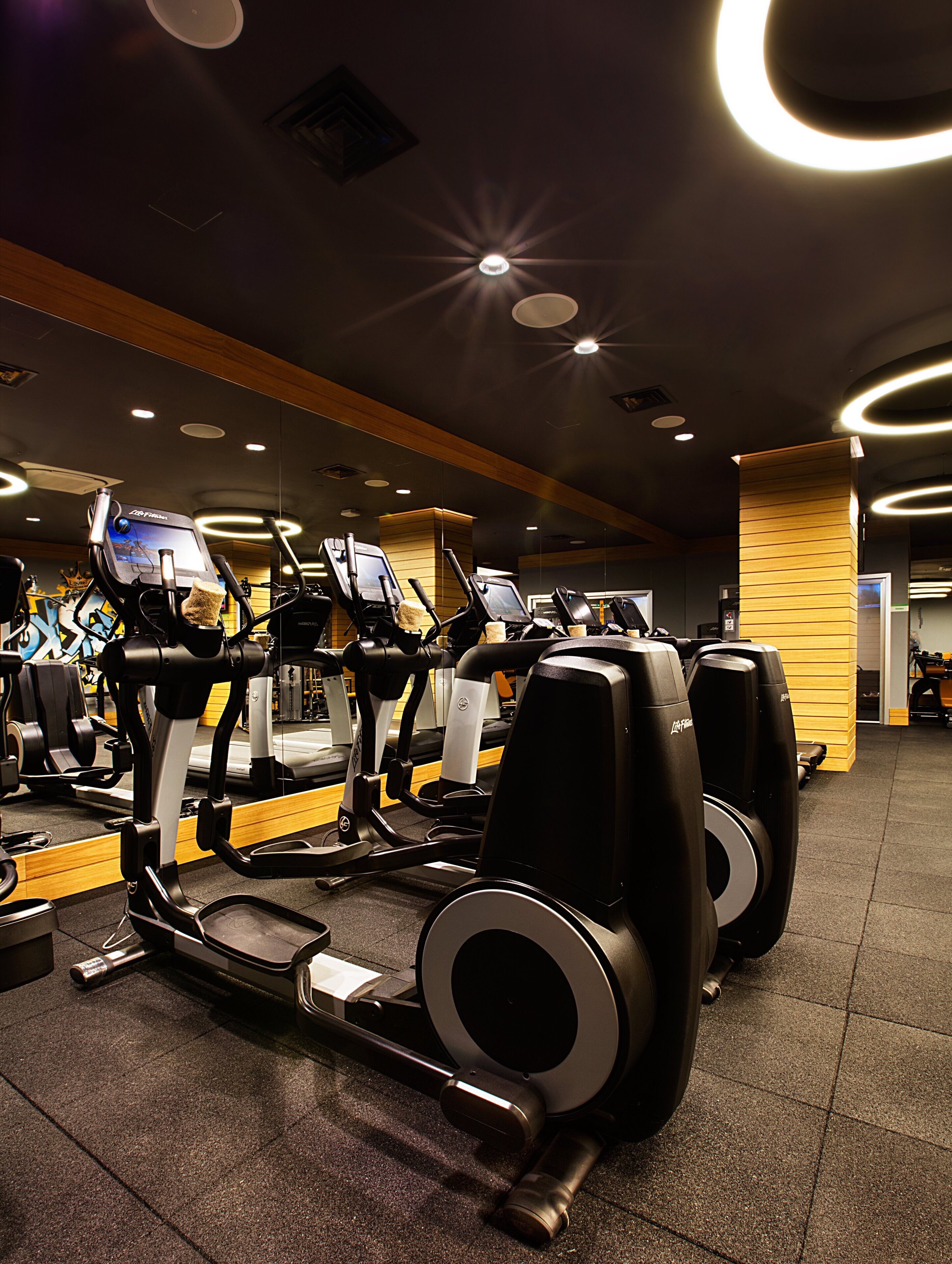 A gym with multiple treadmills, exercise equipment, and a wooden accent wall.
