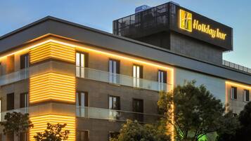 A modern building with a prominent 'Holiday Inn' sign, featuring a flat roof, large windows, and a balcony with glass railings.