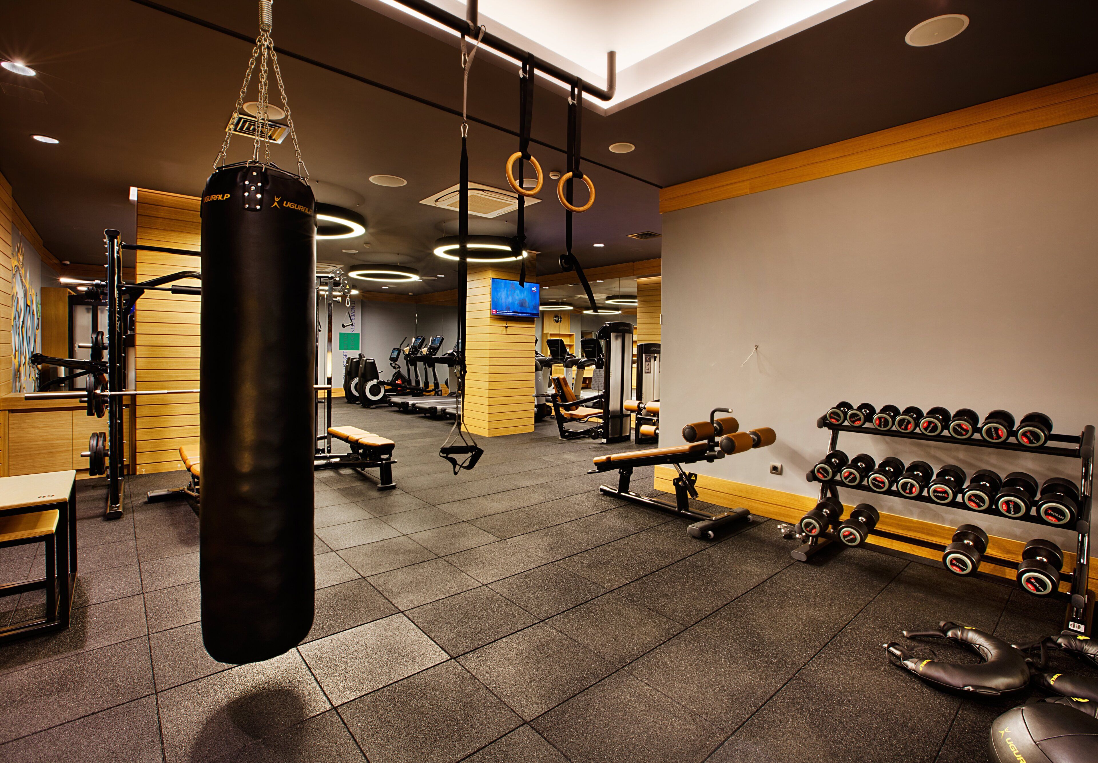 Un gimnasio con saco de boxeo, máquinas de pesas, cintas de correr y una pantalla de televisión.