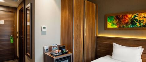 Ein Hotelzimmer mit Bett, Minibar, Holzschrank, einem Bild an der Wand und einem Thermostat.