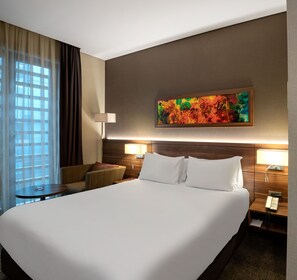 Een hotelkamer met een groot bed, twee nachtkastjes met lampen, een stoel en een raam met gordijnen.