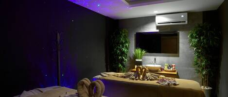 A spa room with two massage tables, a sink, and a mirror.