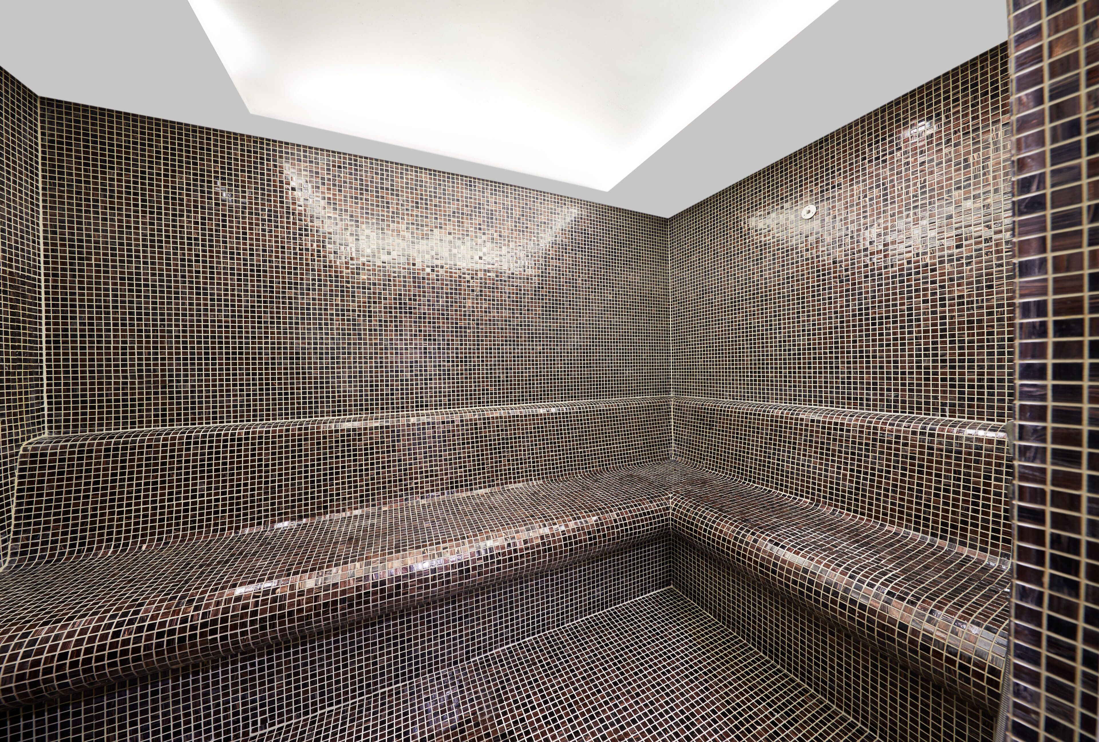 A modern sauna with a geometric tile design and a skylight.