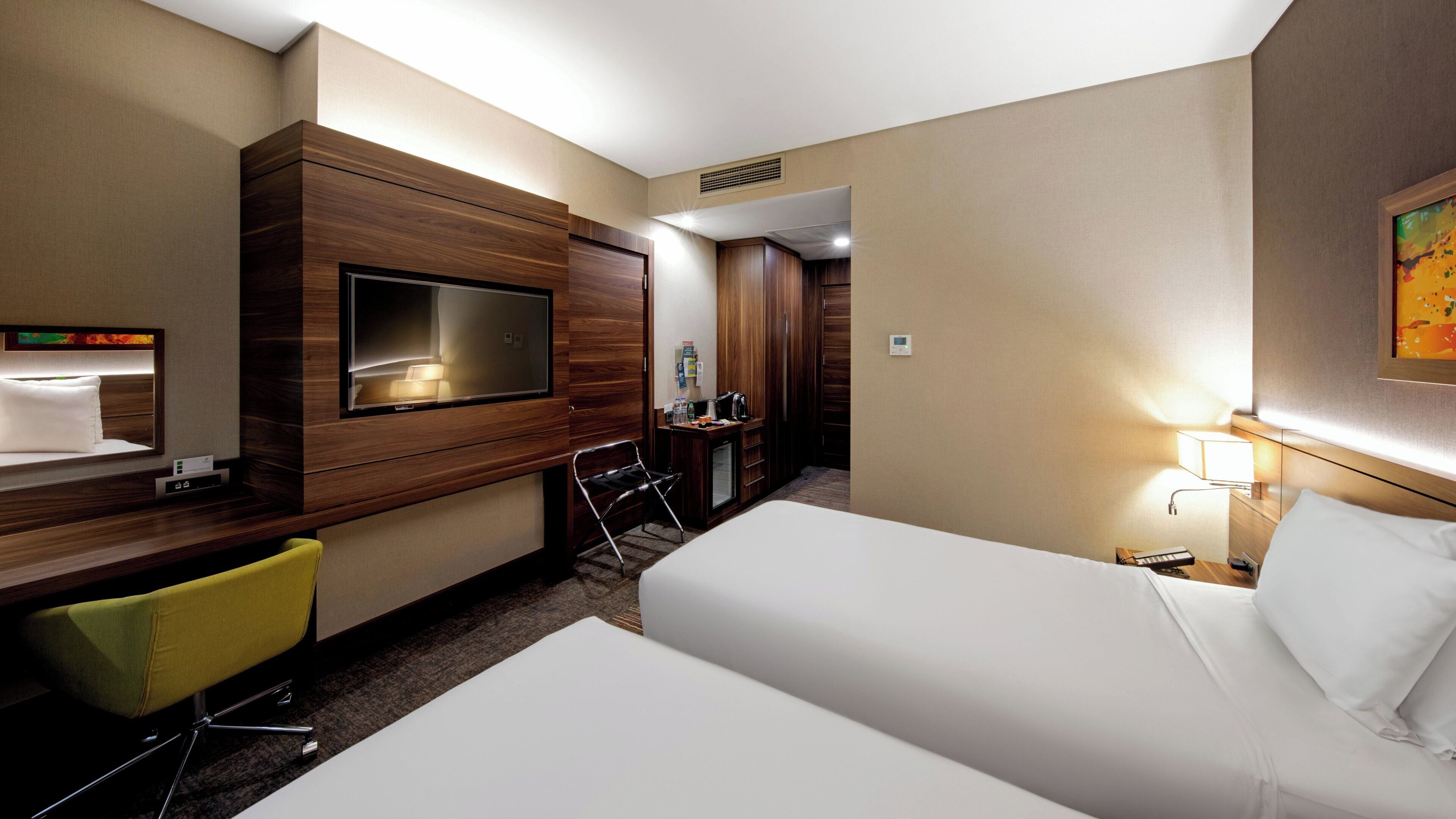 Ein Hotelzimmer mit einem Bett, einem Schreibtisch mit Stuhl, einem an der Wand montierten Fernseher und einem Kleiderschrank.