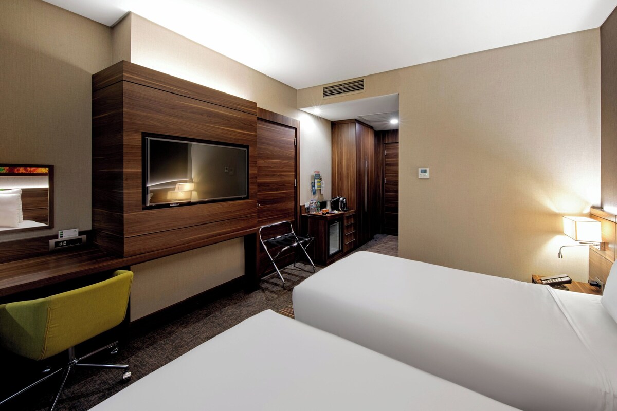 Een hotelkamer met een bed, een bureau met stoel, een aan de muur bevestigde televisie en een kledingkast.