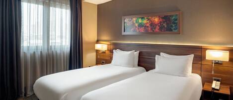 A hotel room with two beds, a large window with sheer curtains, a painting on the wall, and bedside lamps.