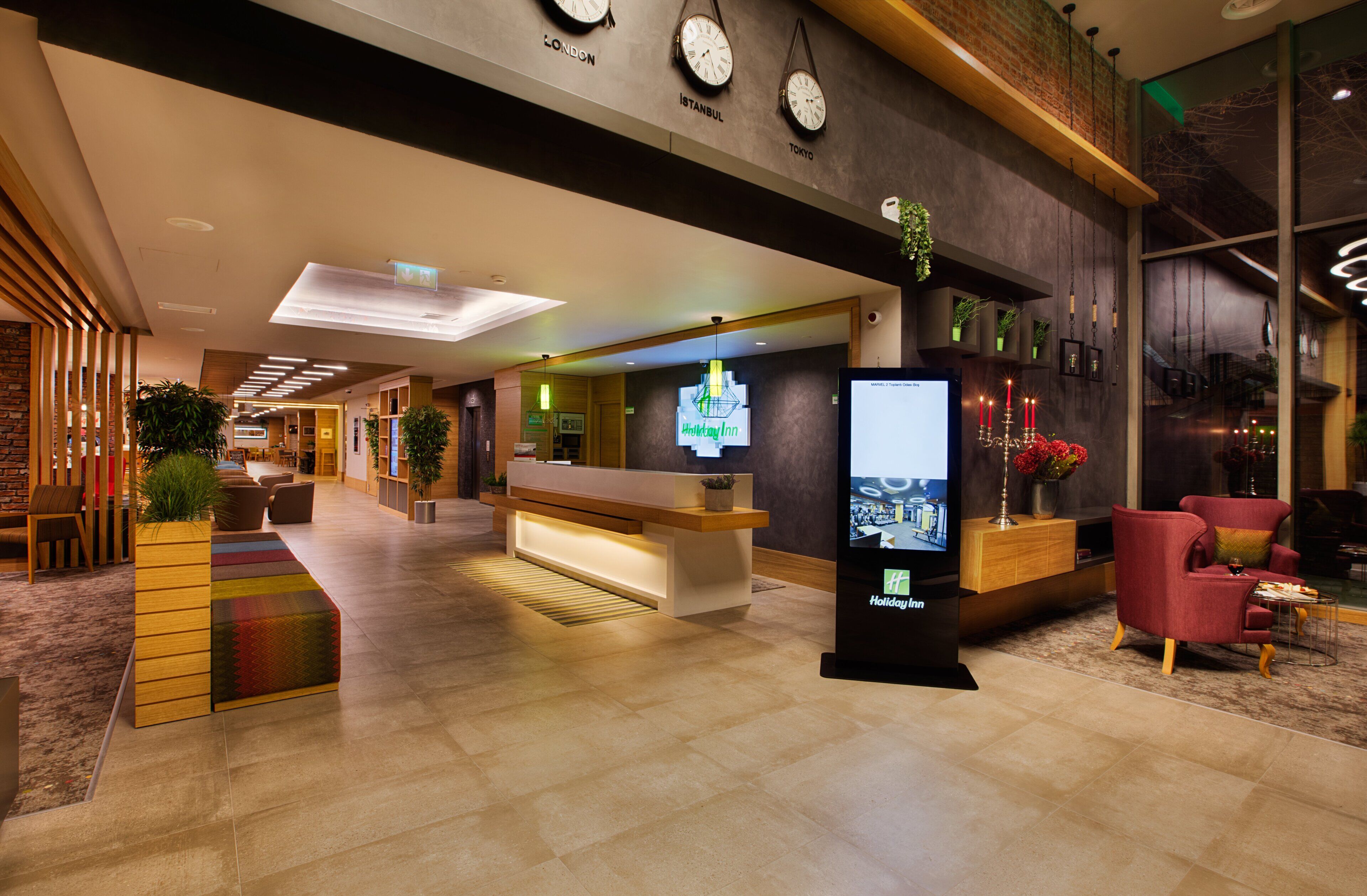 Eine Hotlellobby mit einer Rezeption, einer Sitzecke und einer Wand mit Uhren für verschiedene Städte.