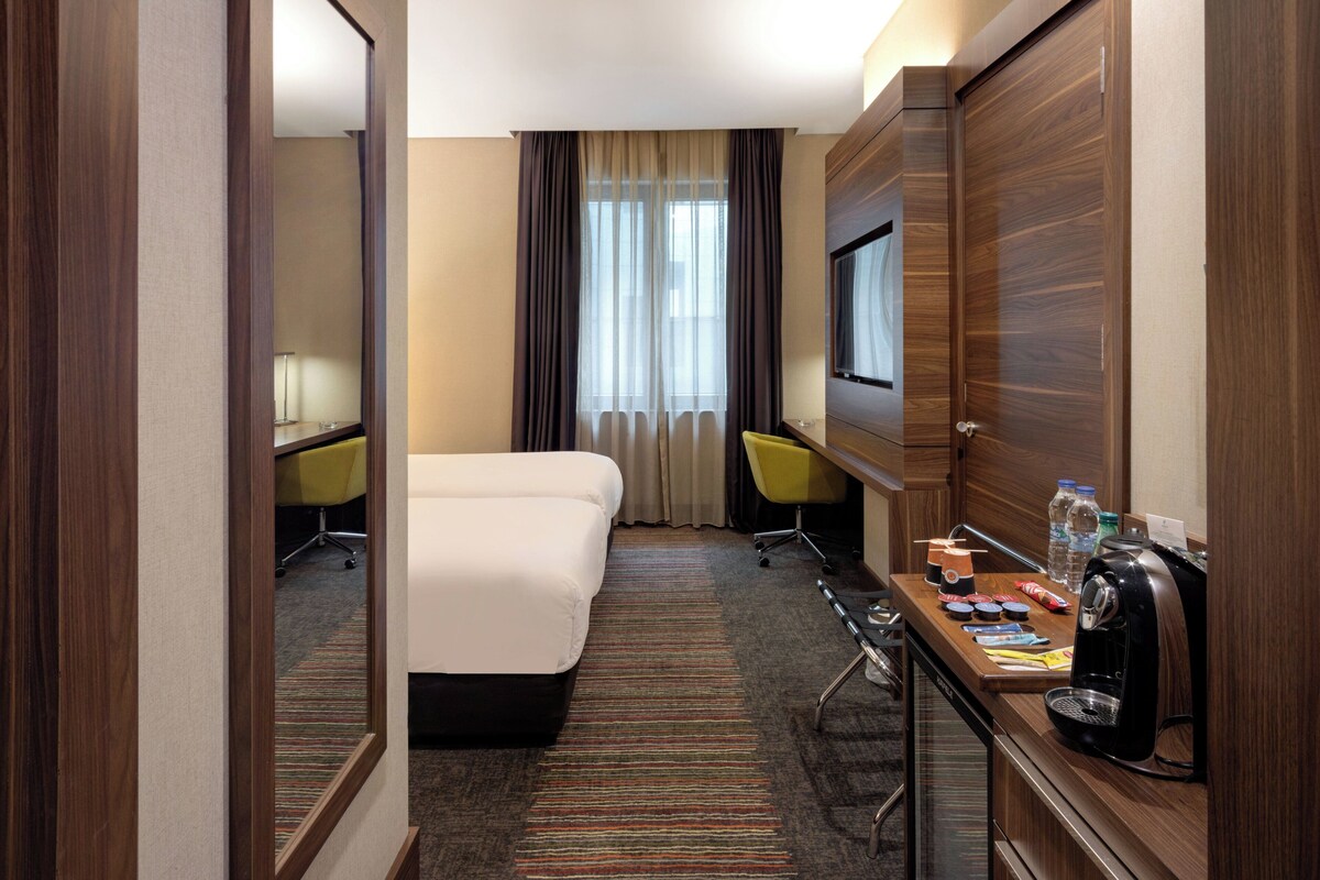 Een hotelkamer met een bed, een bureau met koffiezetapparaat, een stoel en een televisie.