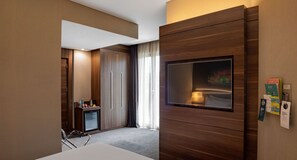 Een moderne hotelkamer met een grote televisie, een minibar en een bureau met stoel.
