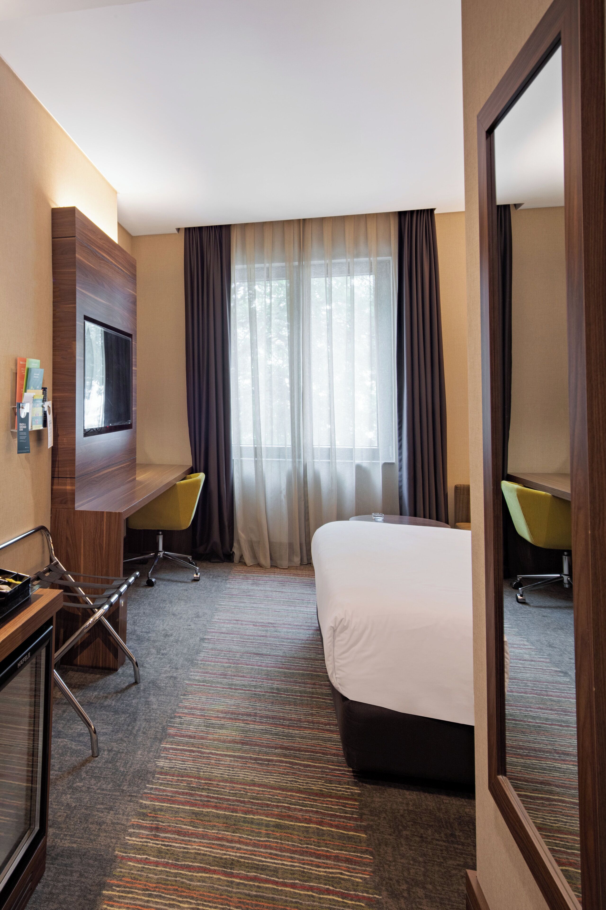 Habitación de hotel con cama, escritorio, dos sillas, televisor y ventana con cortinas.
