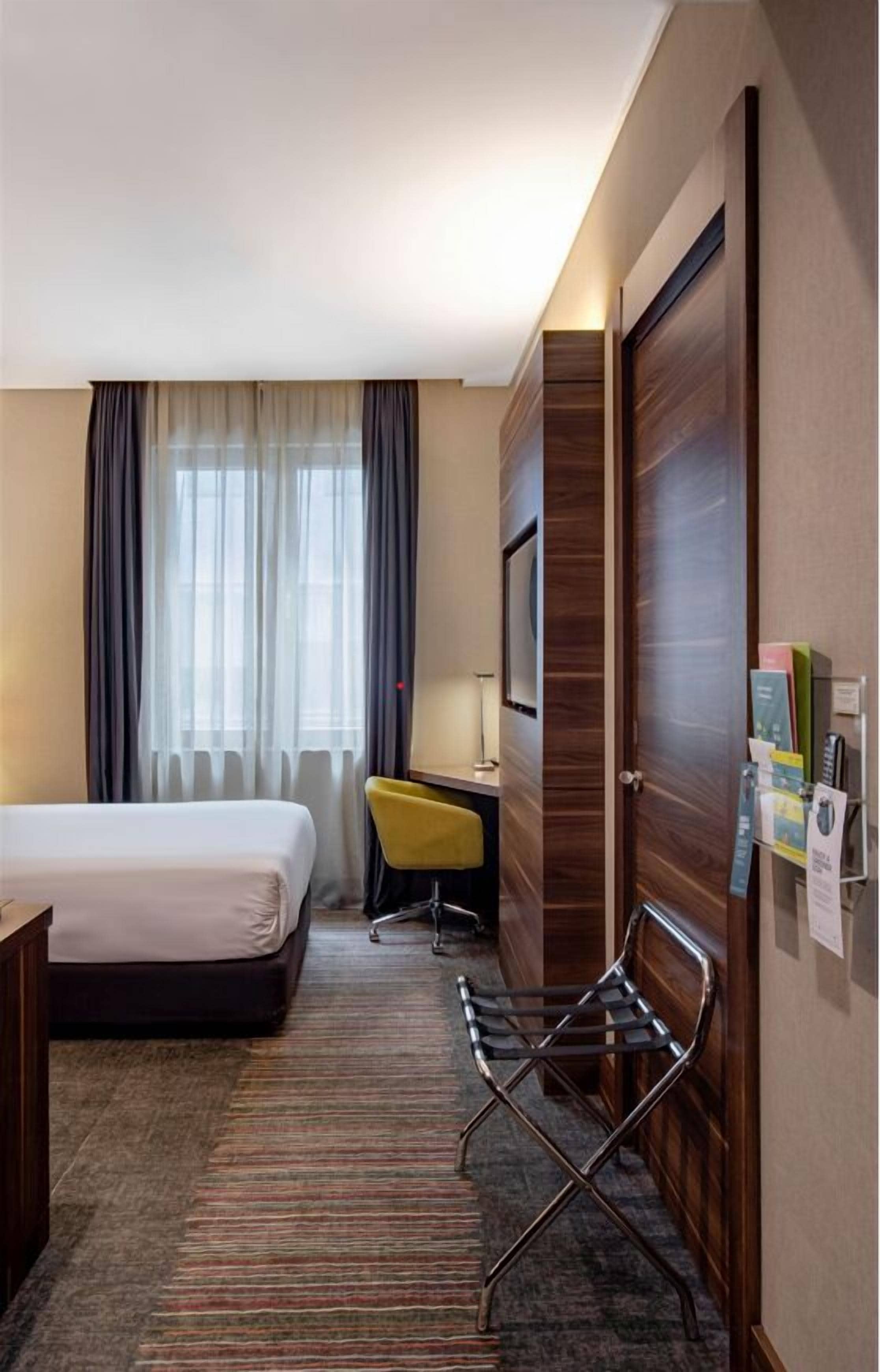 Habitación de hotel con cama, escritorio, silla, televisor y puerta.