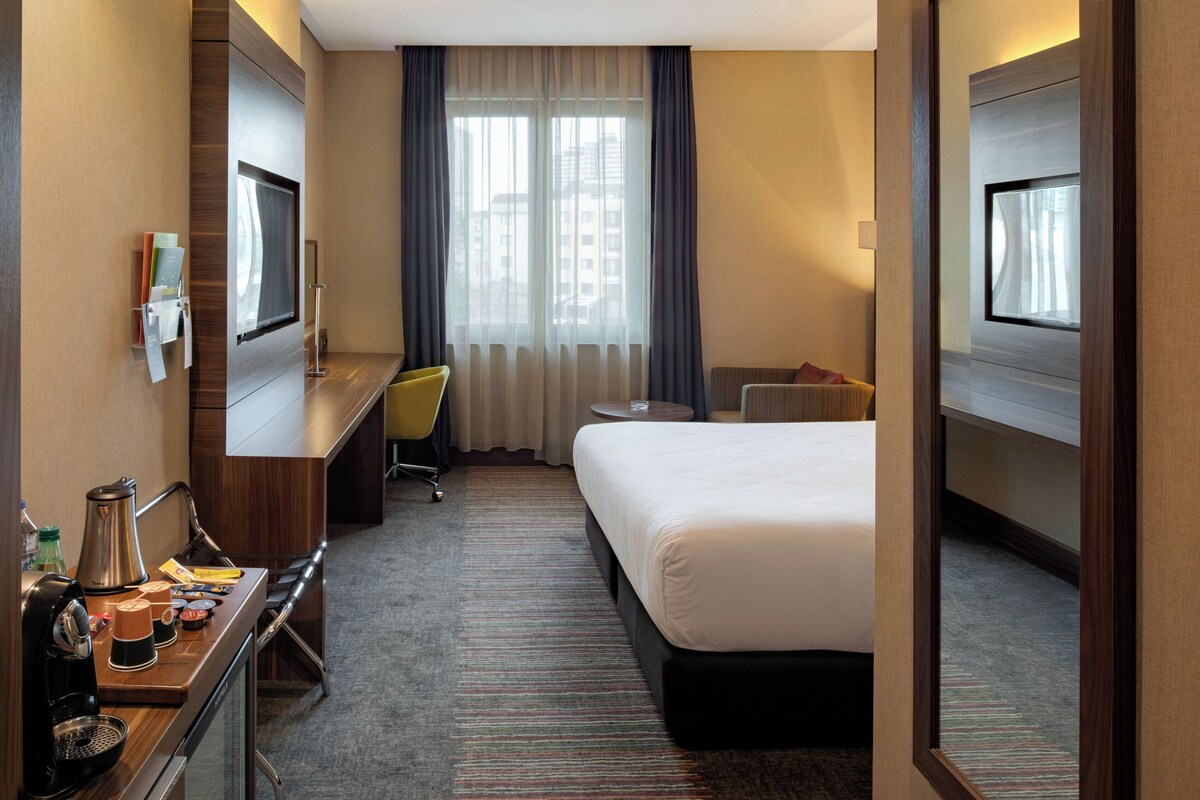 Een hotelkamer met een bed, een bureau met koffiezetapparaat, een stoel en een televisie.