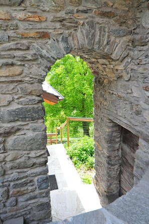 Un arco de piedra que da acceso a un jard ín con un banco de madera y una barandilla de metal.