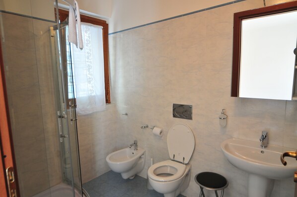 A bathroom with a glass shower enclosure, a bidet, a toilet, a sink, and a mirror.