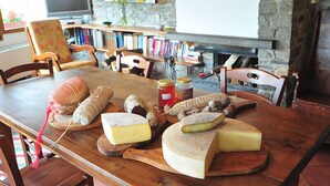 Ein rustikaler Esstisch mit verschiedenen Käsesorten und Wurstwaren, umgeben von Holzstühlen und einem Kamin aus Stein.