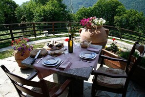 An outdoor dining setup with a table set for two, surrounded by chairs, with a scenic mountain view in the background. - Agriturismo La Fonte di Mariella (Dosso del Liro)