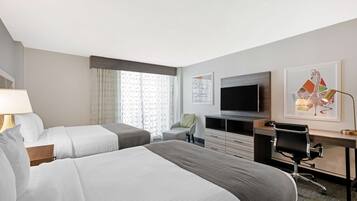 A hotel room with two beds, a desk, a chair, a TV, and artwork on the walls.