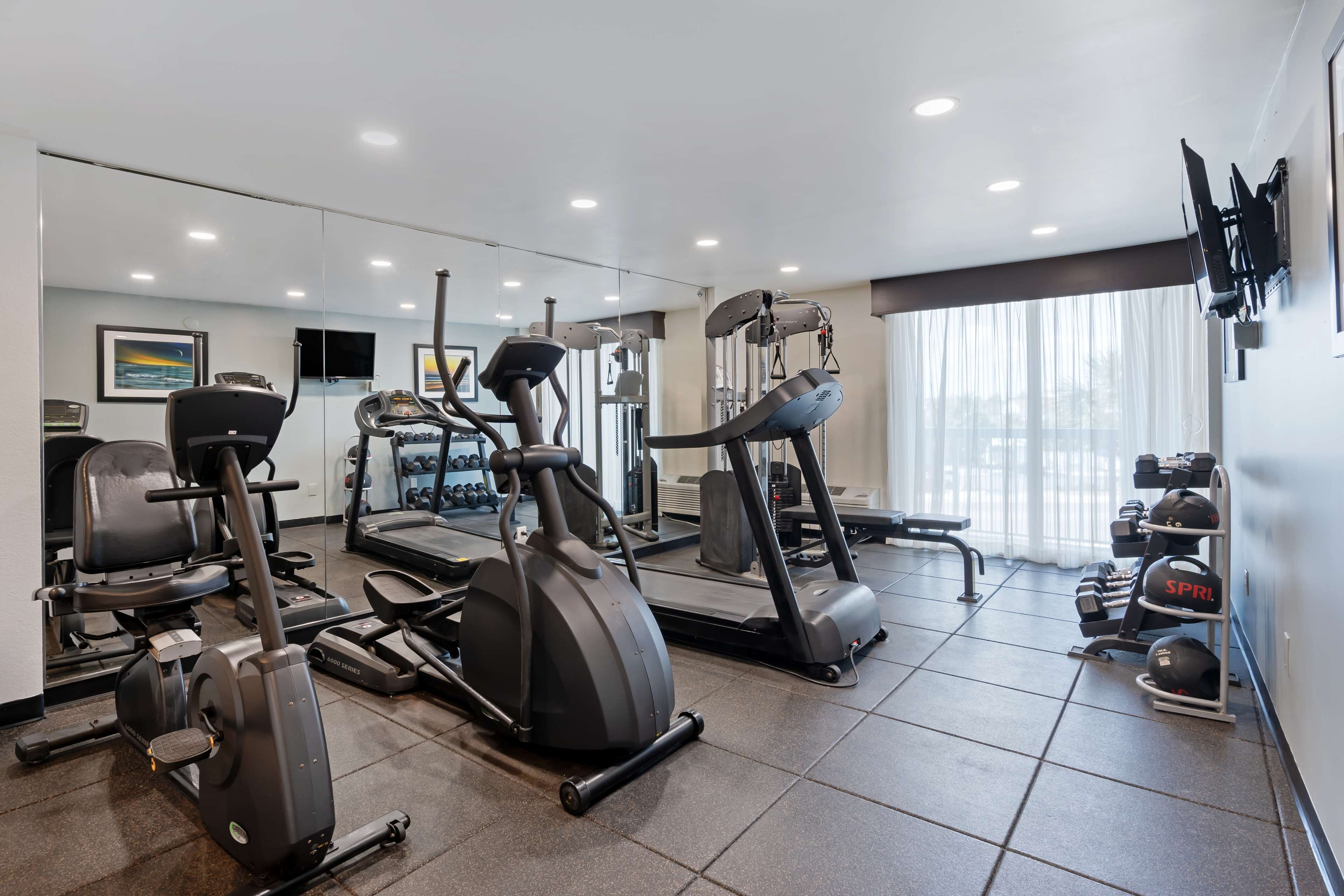 A modern gym with various cardio machines, weightlifting equipment, and a large mirror.