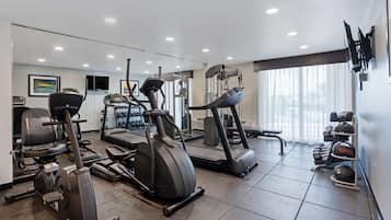 Un gimnasio moderno con diferentes máquinas de cardio, equipo de levantamiento de pesas y un espejo grande.