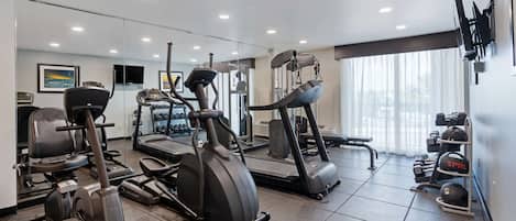 Un gimnasio moderno con diferentes máquinas de cardio, equipo de levantamiento de pesas y un espejo grande.