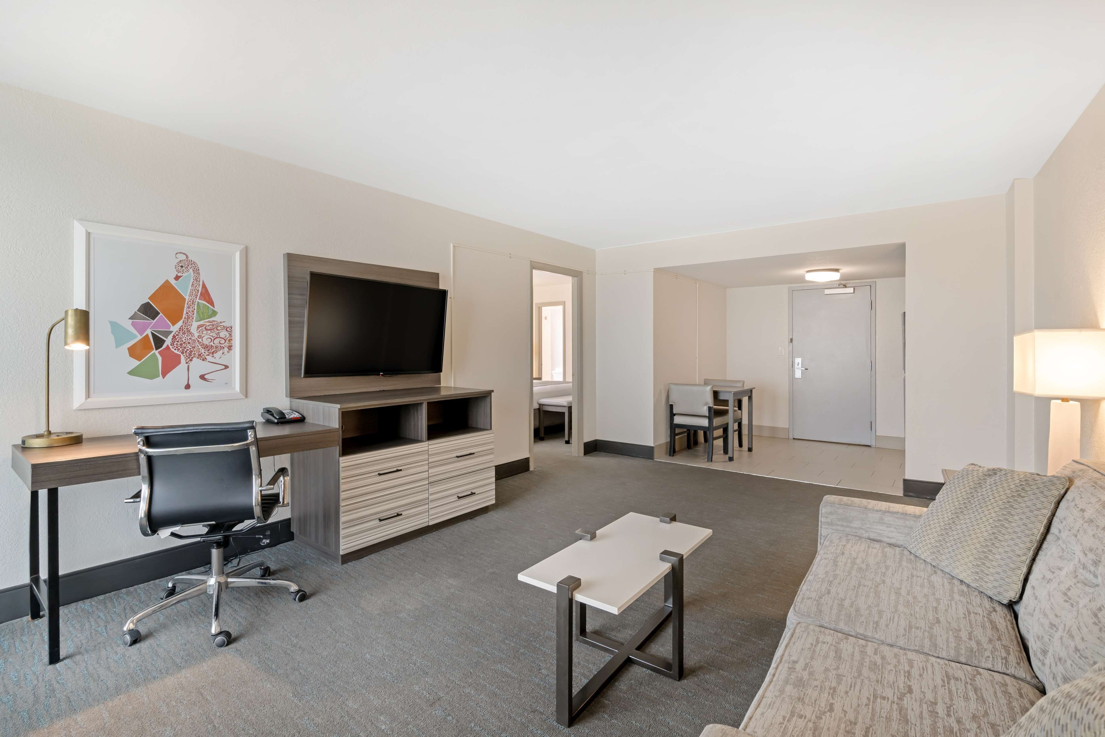 A modern hotel room with a flat-screen TV, a desk with a chair, a sofa, and a small table.
