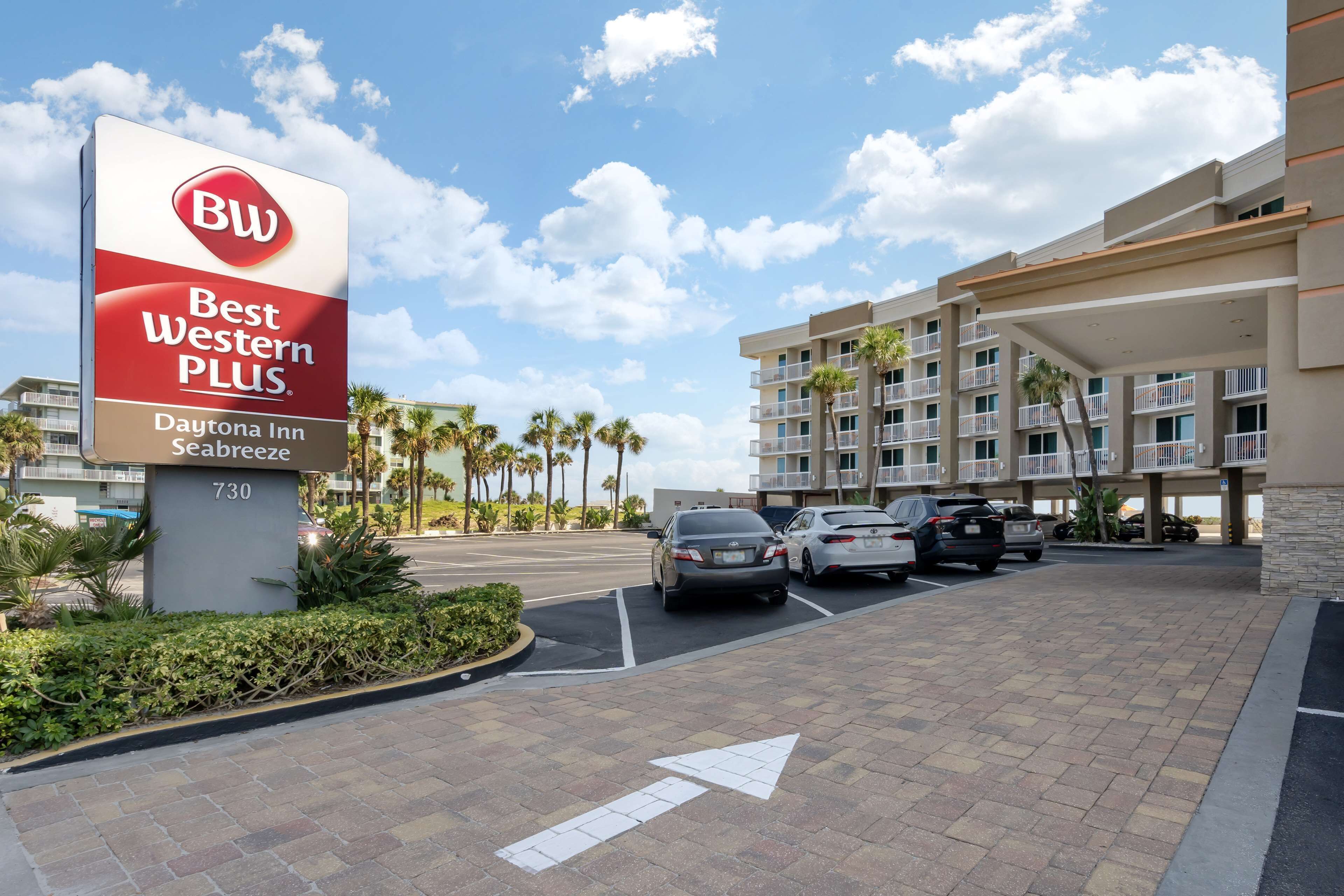 A Best Western Plus sign at Daytona Inn Seabreeze, with a parking lot and a multi-story building with balconies.