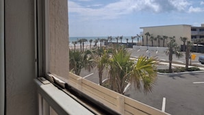 A view from a window overlooking a parking area with palm trees and a building in the background.