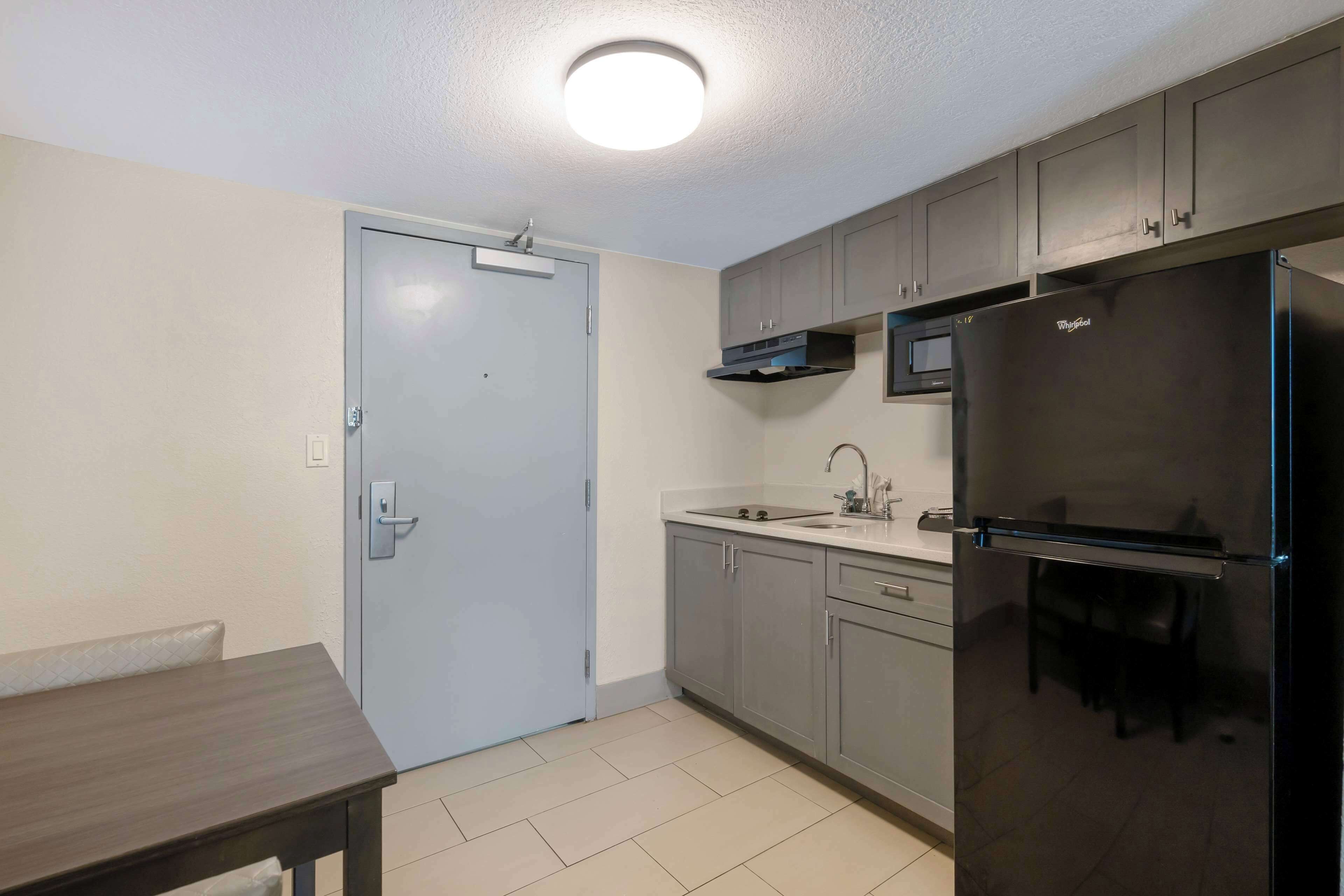 A compact kitchen with grey cabinets, a stainless steel refrigerator, a microwave, and a sink.