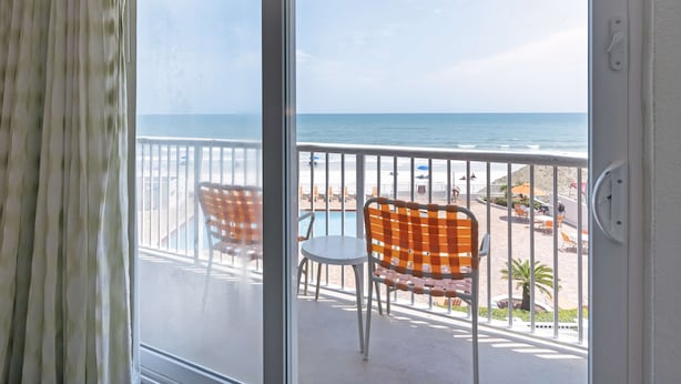 A balcony with a view of the beach, featuring two chairs and a table.