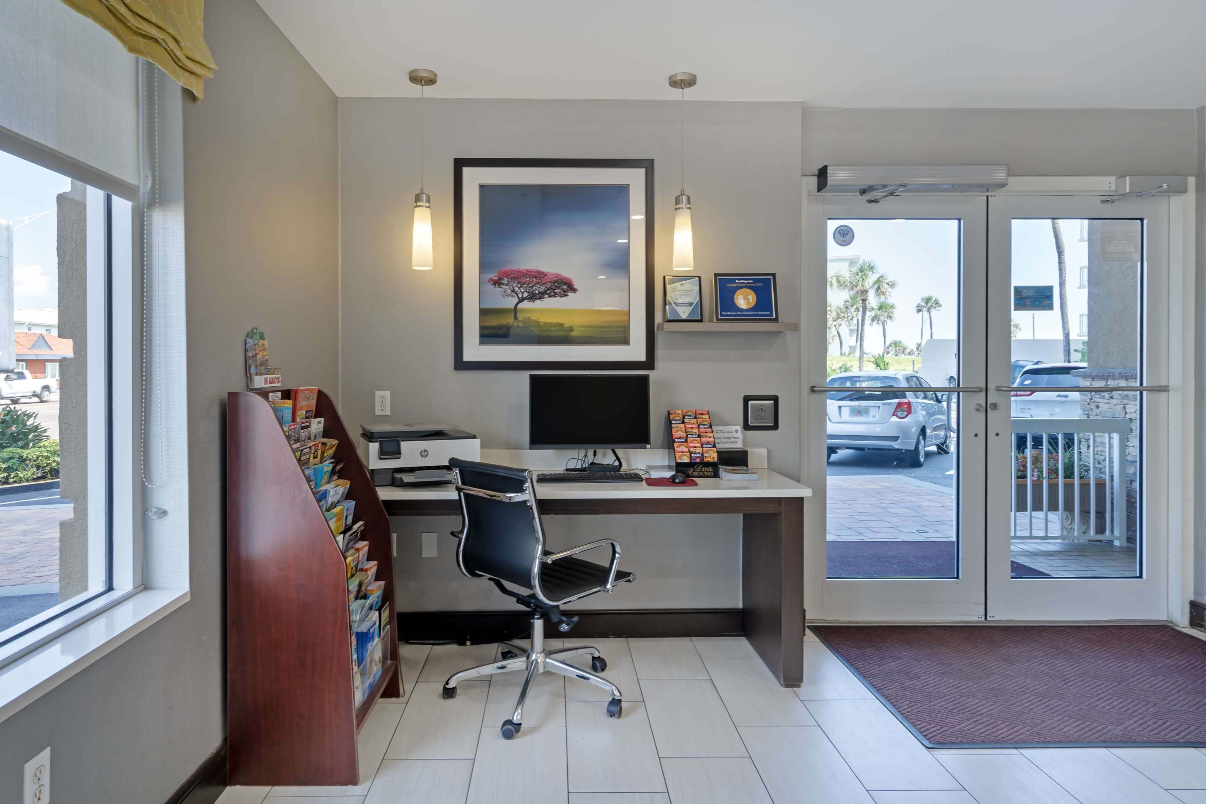 A hotel reception area with a desk, computer, framed picture, and a view of the parking area.