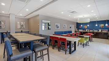 A modern dining area with multiple tables and chairs, a counter with a menu, and artwork on the walls.