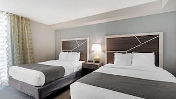 A hotel room with two beds, a nightstand with a lamp, and a window with curtains.