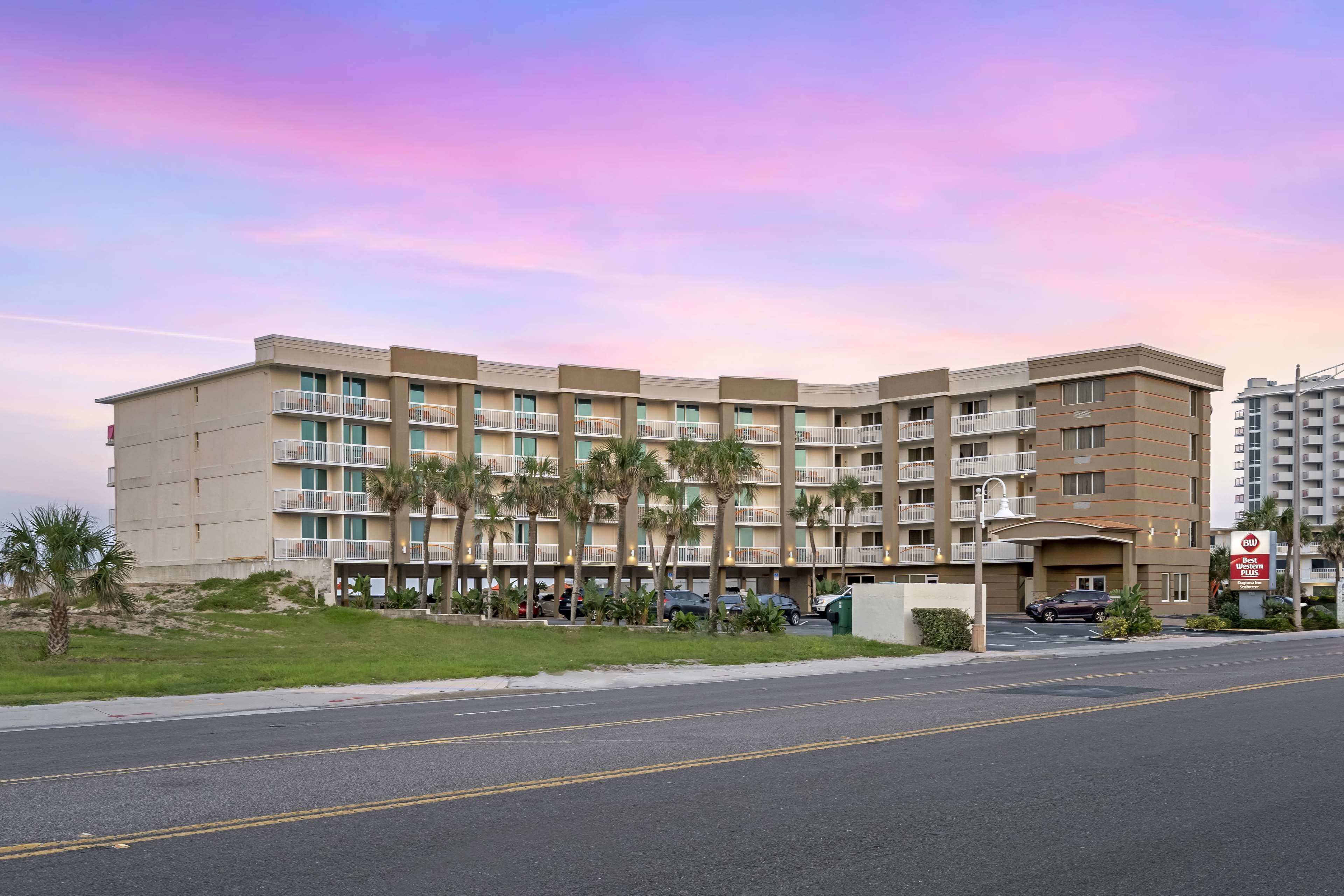 A multi-story hotel with balconies, palm trees, and a parking area.