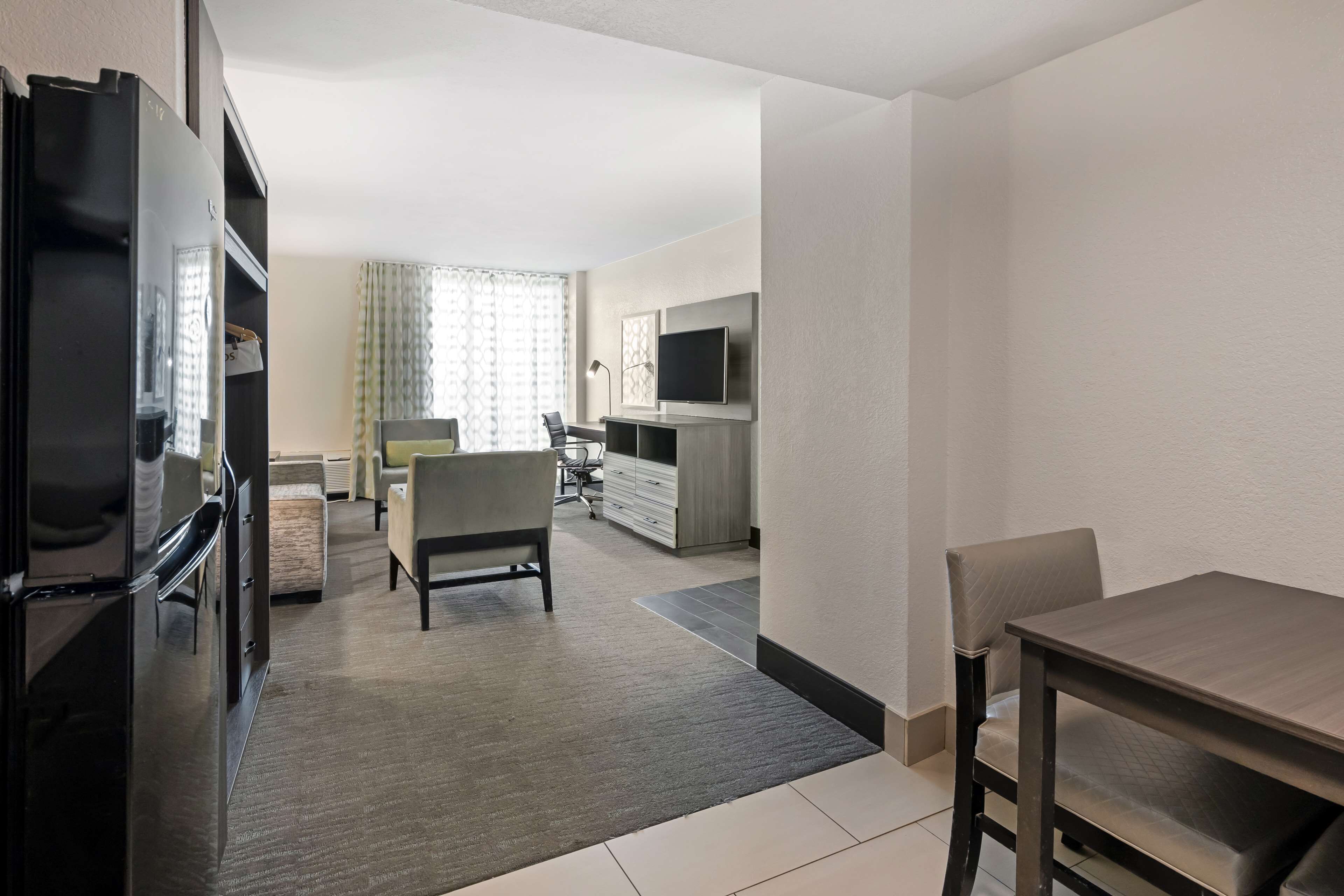 A modern hotel room with a kitchenette, a dining area, and a TV mounted on the wall.