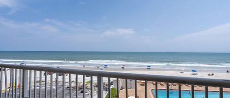 A balcony with a view of the beach and a pool.