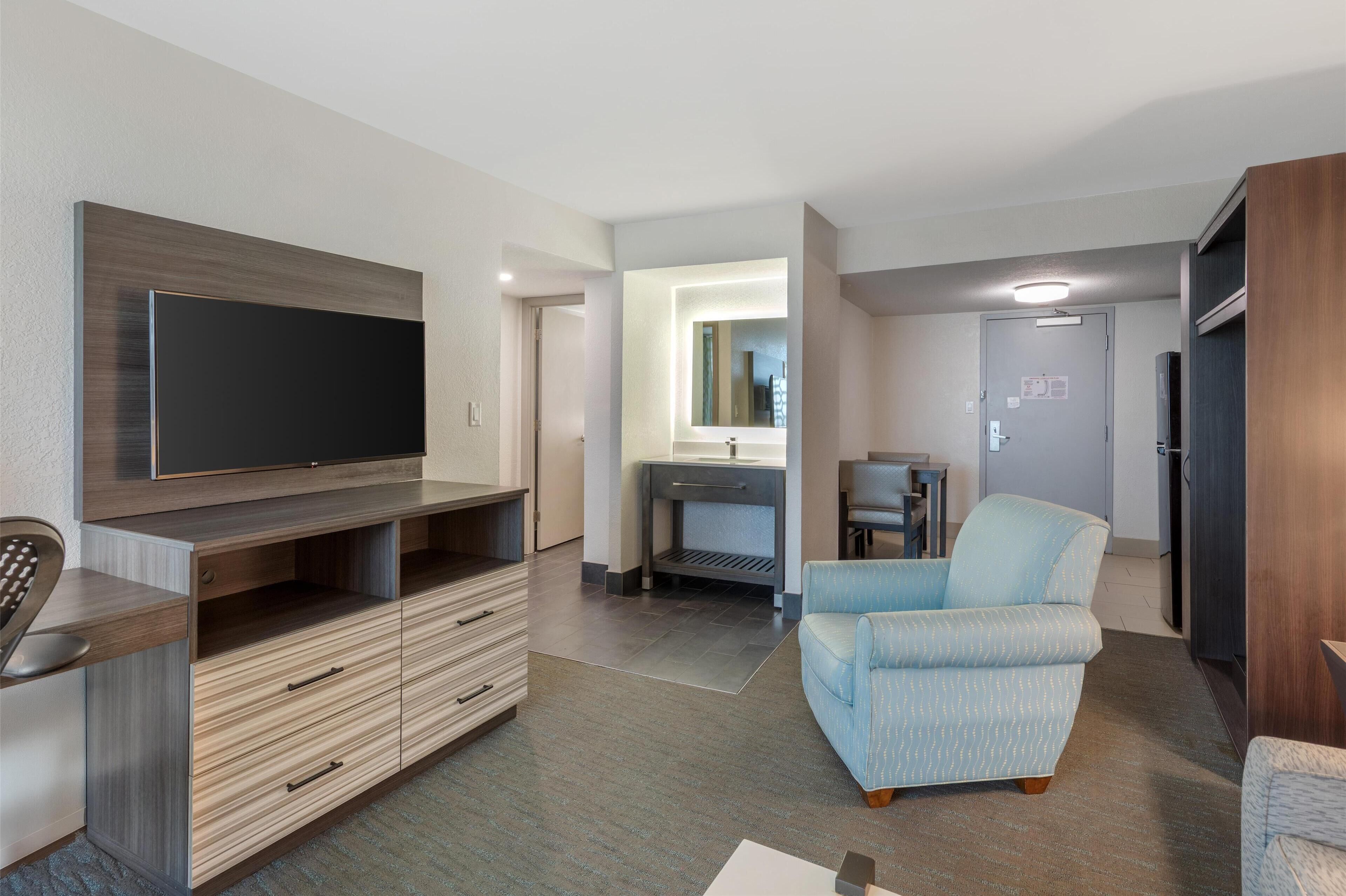 Una sala de estar moderna con un televisor de pantalla plana, un mueble bajo de madera y un sillón azul claro.