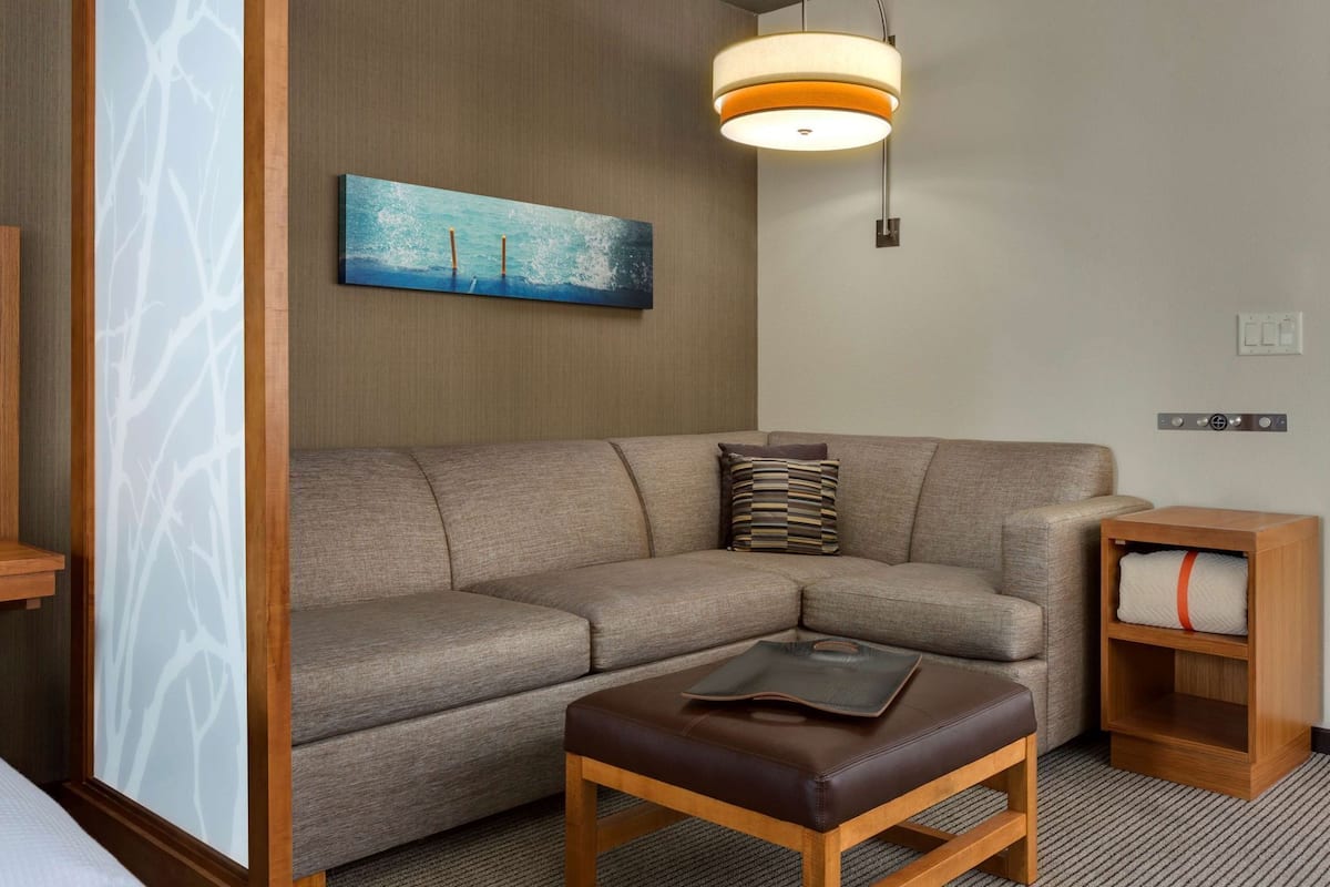A modern living room with a sectional sofa, a wooden coffee table, a wall-mounted light fixture, and a small wooden side table.