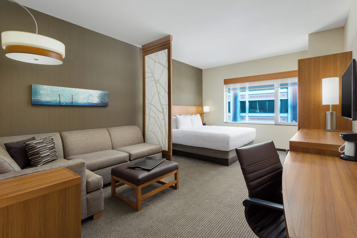 A hotel room with a bed, a sofa, a desk, and a television.