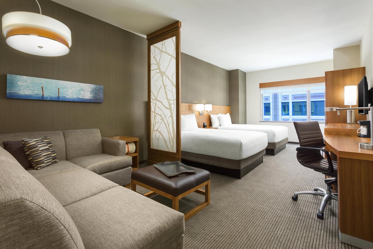 A hotel room with a sofa, a desk, a bed, and a large window.