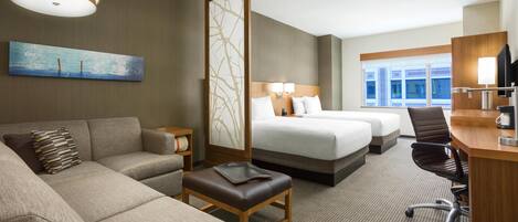 A hotel room with a sofa, a desk, a bed, and a large window.
