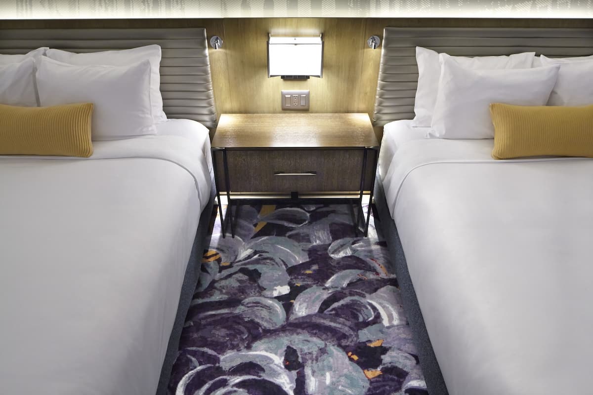 Una habitación de hotel con dos camas, una mesita de noche, una pequeña mesa y una alfombra estampada.