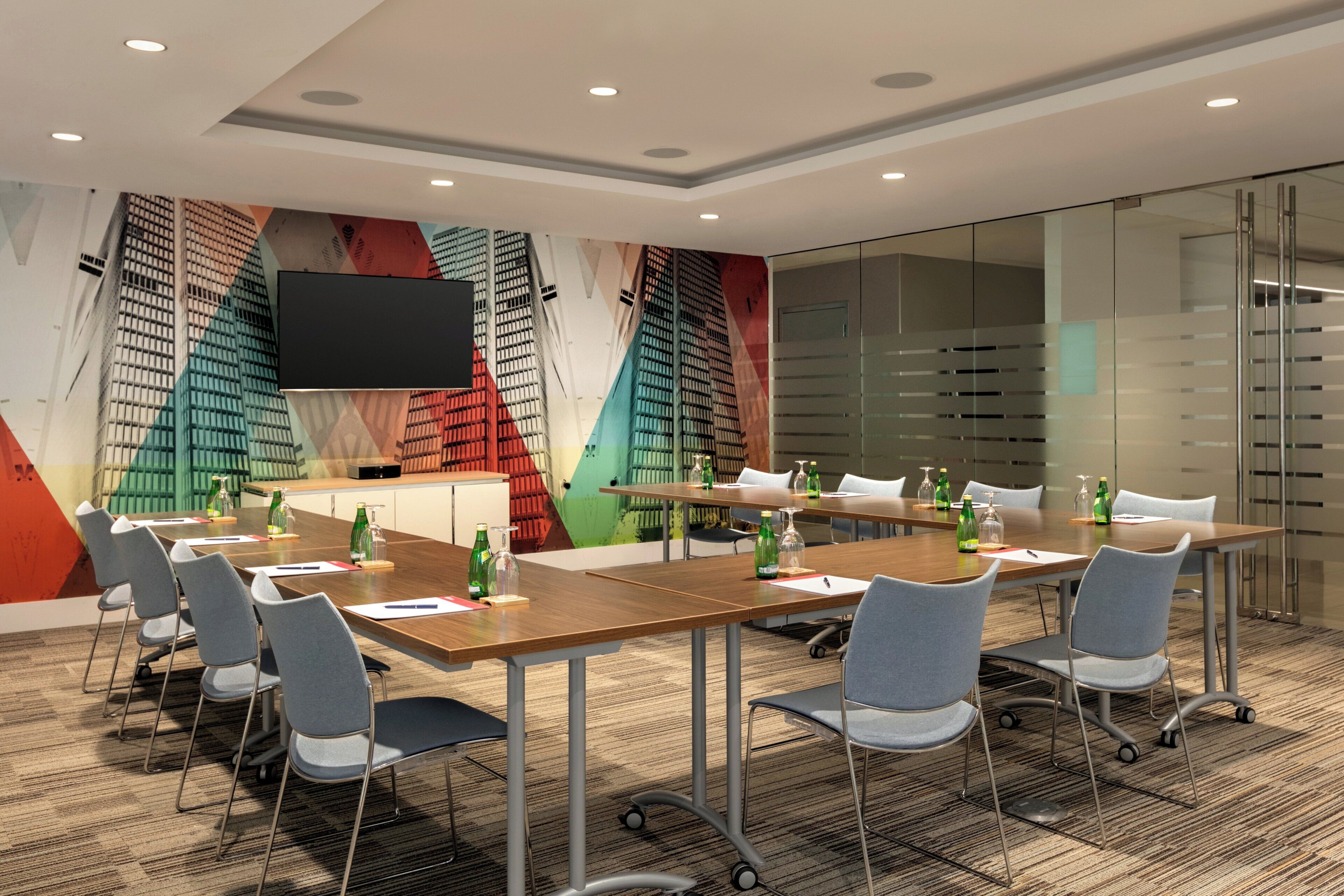 A conference room with a long table, chairs, and a glass partition.