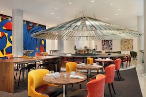 Un restaurante moderno con barra central, mesas redondas y arte abstracto vibrante en las paredes.
