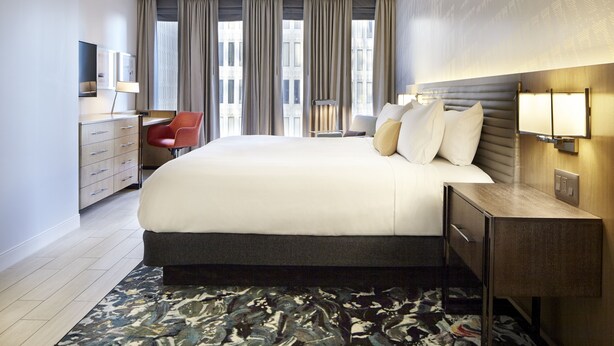 A modern hotel room with a large bed, a desk, a chair, and a view of the city through large windows. - Hotel Indigo Atlanta Downtown by IHG (Atlanta)