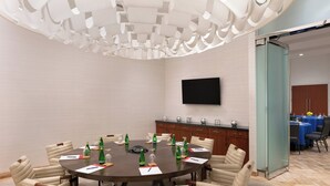 Un salón de conferencias con una mesa redonda, sillas, un televisor de pantalla plana y un panel de vidrio.