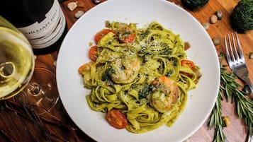 A plate of pasta with shrimp and vegetables, a bottle of wine, and a fork on a wooden table.