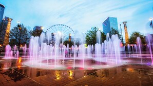 A fountain with water jets, a Ferris wheel, and modern buildings in the background. - Hotel Indigo Atlanta Downtown by IHG (Atlanta)
